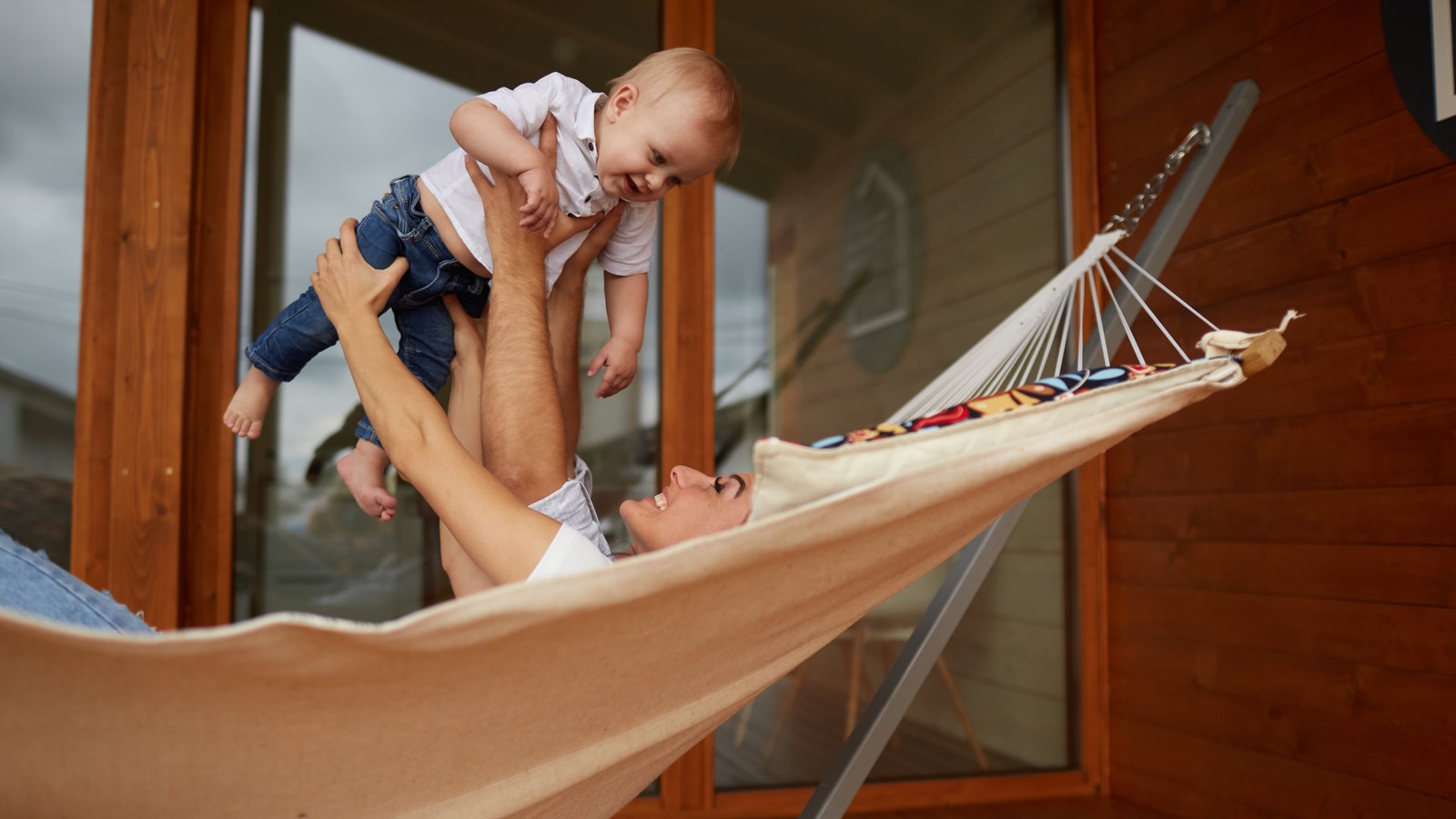 A relaxed family lounging outdoors while monitoring their baby sleeping peacefully in a portable travel crib nearby.