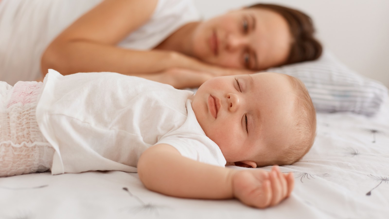 Loving mother resting next to sleeping infant daughter during scheduled developmental nap